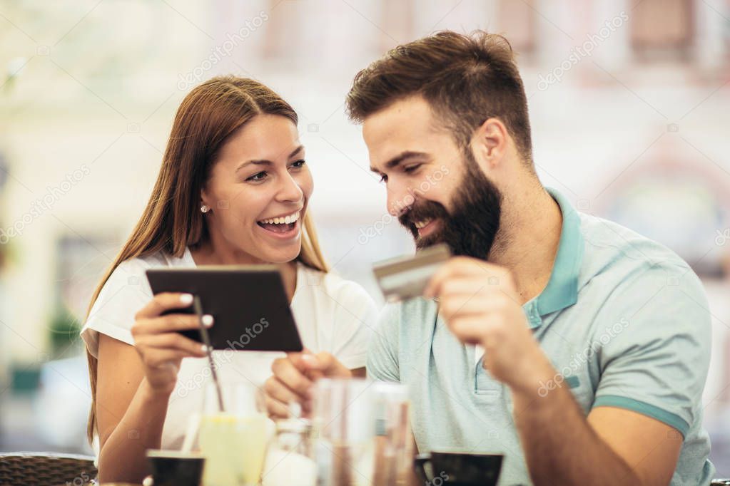 Couple having coffee on a date, using digital tablet and credit card for online shopping