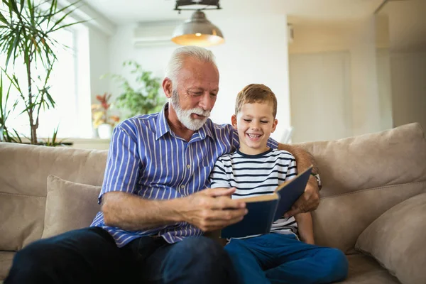 Grandfather with grandson reading together on sofa