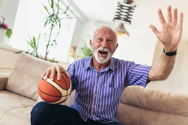 Senior man cheering for basketball game and holding basketball ball