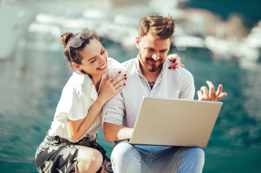 Güzel romantik çift dizüstü bilgisayar kullanarak. Belgili tanımlık laptop resimleri, arka plan üzerinde tekne ile turistik deniz tatil liman tarafından seyahat ederken izlerken.