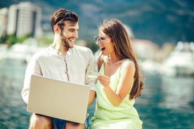 Arka plan üzerinde tekne ile turistik deniz tatil liman tarafından laptop ve kredi kartı kullanarak güzel romantik çift