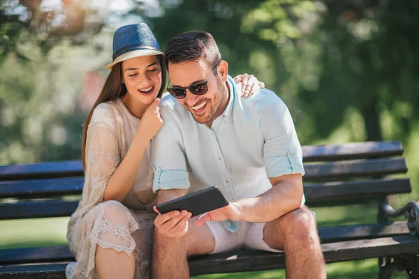 快乐的年轻夫妇使用智能手机坐在长凳上户外乐趣 — 图库照片