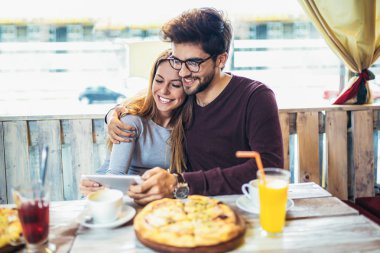 Pizza zevk ve kullanarak gülümseyen iki tablet pc cafe  