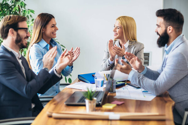 Счастливая группа бизнесменов хлопает в ладоши, сидя за столом в офисе
