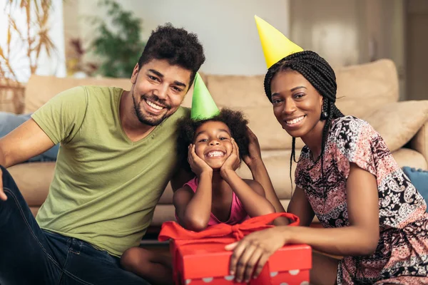 Happy black family at home. African american father, mother and child celebrating birthday, having fun at party. Young woman giving gift to daughter