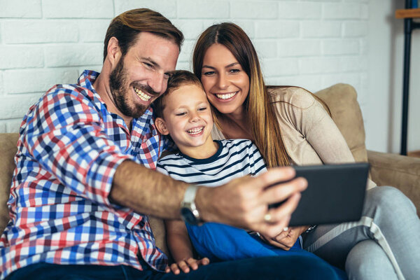 Happy family using digital tablet taking selfie at home, and having fun.