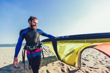 Yakışıklı beyaz adam profesyonel sörfçü onun uçurtma ile kumlu plajda durup