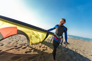 Yakışıklı beyaz adam profesyonel sörfçü onun uçurtma ile kumlu plajda durup