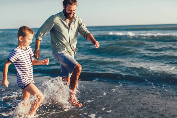 Happy father and son, man & boy child, running and having fun in the sand and waves of a sunny beach