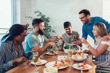 Grup mutlu genç arkadaşlar evde akşam yemeği zevk. Akşam yemeği tadını çok ırklı arkadaş grubu