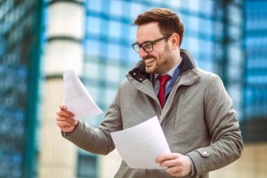 Belgeler, kağıtları tutan genç çekici bir iş adamı. Genç adam açık havada kentsel alanda belgeleri okuma konsantre.