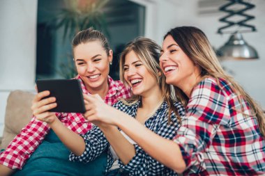 Dijital kullanarak üç arkadaşlarım birlikte tablet. Eğleniyor koltukta oturan kadınlar akıllı dijital pc tablet modern cihaz kullanarak internette sörf