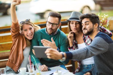 Grup dört arkadaşıyla birlikte bir kahve içer. İki kadın ve iki erkek gülüyor ve dijital tablet kullanarak zamanlarını zevk Café.