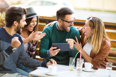 Grup dört arkadaşıyla birlikte bir kahve içer. İki kadın ve iki erkek gülüyor ve dijital tablet kullanarak zamanlarını zevk Café.