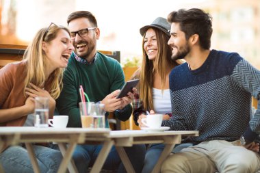 Grup dört arkadaşıyla birlikte bir kahve içer. İki kadın ve iki erkek gülüyor ve dijital tablet kullanarak zamanlarını zevk Café.