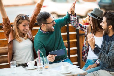 Grup dört arkadaşıyla birlikte bir kahve içer. İki kadın ve iki erkek gülüyor ve dijital tablet kullanarak zamanlarını zevk Café.