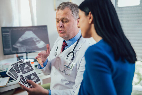Gynecologist doctor showing ultrasound image to pregnant woman at hospital