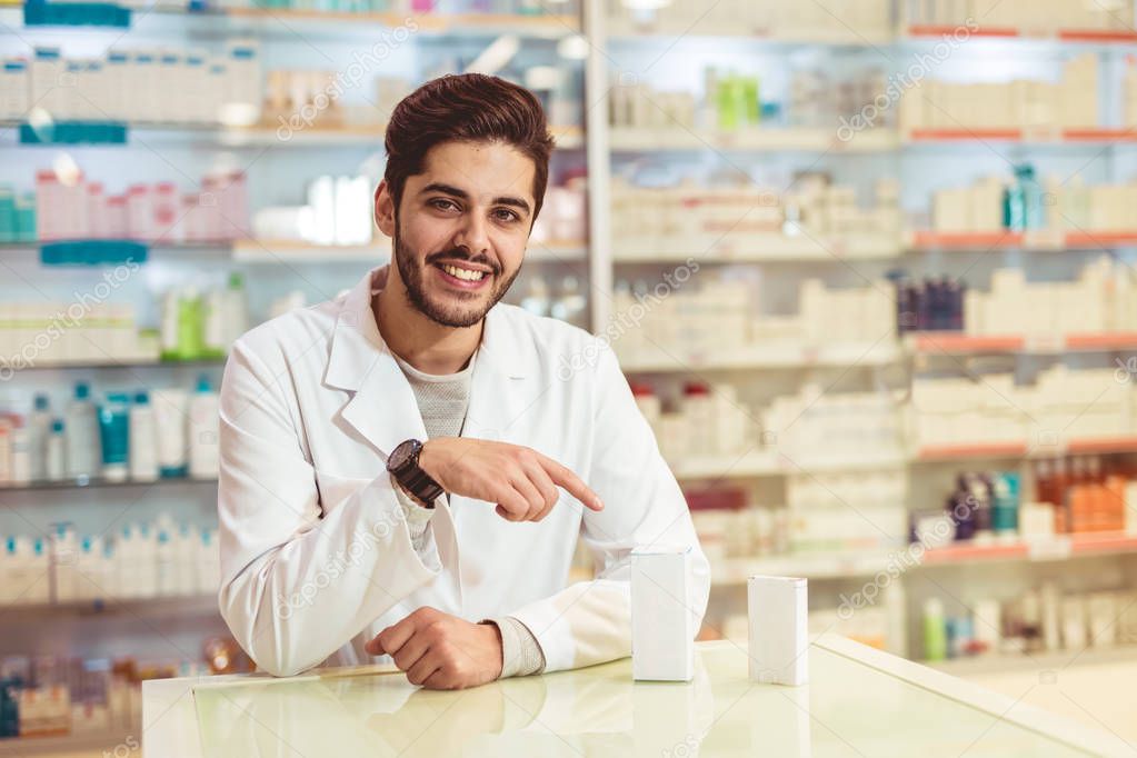 Friendly male pharmacist dispensing medicine holding a box of tablets