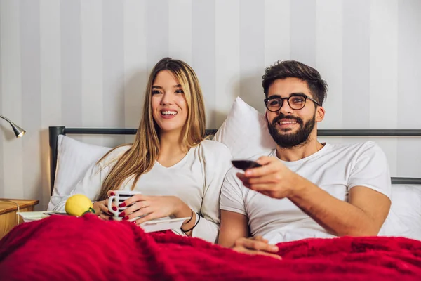 Beautiful young couple watching TV in Bed.