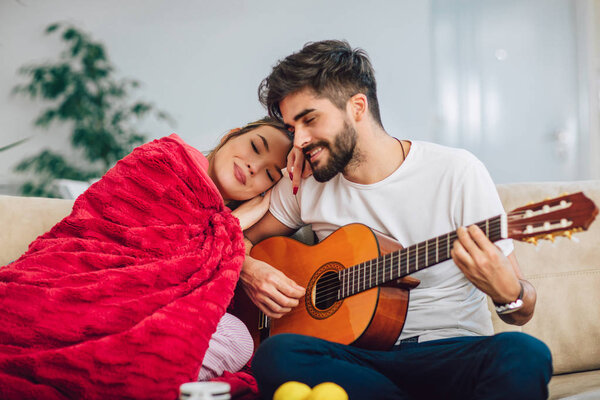 Young couple are playing guitar and happy smiling while sitting on couch at home