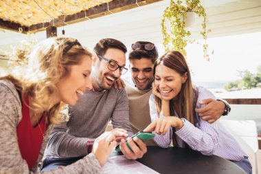 Grup dört arkadaşıyla birlikte bir kahve eğleniyor. İki kadın ve iki erkek gülüyor ve akıllı telefon kullanarak Café.