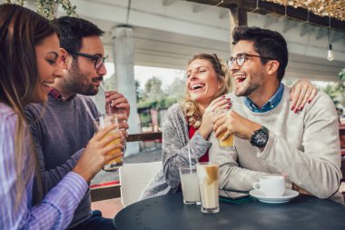 Bir grup arkadaş birlikte kahve içiyorlar. İki kadın ve iki erkek kafede gülüp eğleniyorlar.