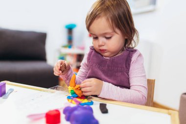 Çocuk kız çocuk odası Oda masada otururken hamuru ile oynuyor.