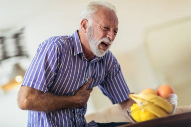 Senior man suffering from heart attack at home clipart