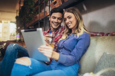 Mutlu genç çift dijital tablet birlikte bir kahve dükkanında kullanma portresi. Genç adam ve kadın bakarak dokunmatik ekran bilgisayar ve gülümseyen.