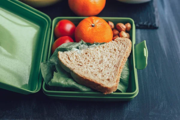 School lunch boxes with sandwich and fresh vegetables, nuts and fruits on blackbackground. Healthy eating concept.