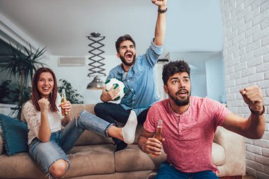 Mutlu arkadaşlar ya da futbol taraftarları televizyonda maç izleyip zaferi evde kutluyorlar. Dostluk, spor ve eğlence kavramı..