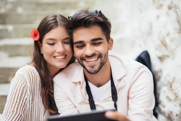 Romantic couple sitting on stairs and looking at tablet computer