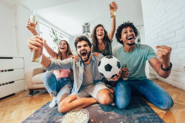 Mutlu arkadaşlar ya da futbol taraftarları televizyonda maç izleyip zaferi evde kutluyorlar. Dostluk, spor ve eğlence kavramı..