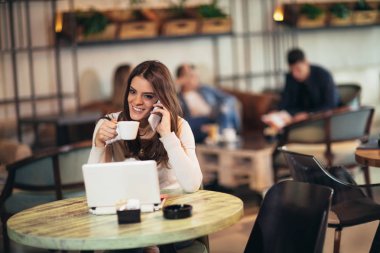 Açık dizüstü bilgisayar telefon kullanarak bar cafe önünde oturan genç kadın
