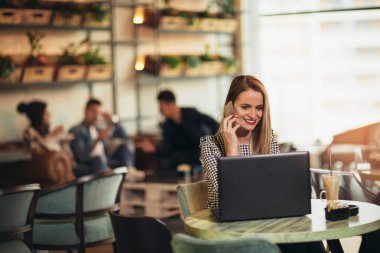 Açık dizüstü bilgisayar telefon kullanarak bar cafe önünde oturan genç kadın