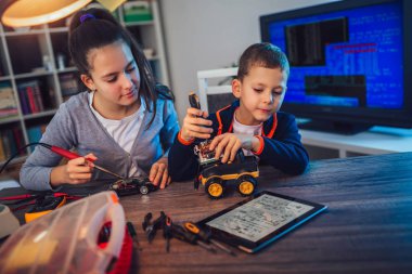 Mutlu gülümseyen erkek ve kız teknik robot oyuncak ve yapmak oluşturur. Tablo ayrıntılarını tam teknik oyuncak