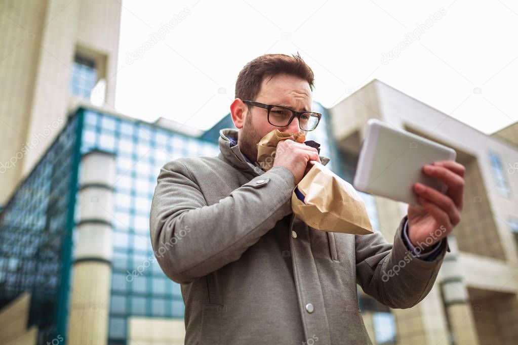 Businessman holding paper bag over mouth as if having a panic attack and looking in digital tablet.