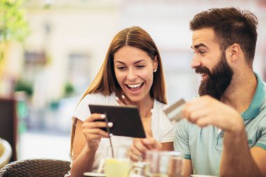 Randevularında kahve içen güzel bir çift online alışveriş için dijital tablet ve kredi kartı kullanıyor.