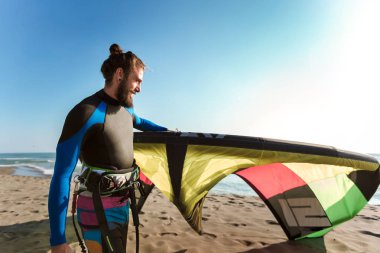 Yakışıklı beyaz adam profesyonel sörfçü onun uçurtma ile kumlu plajda durup