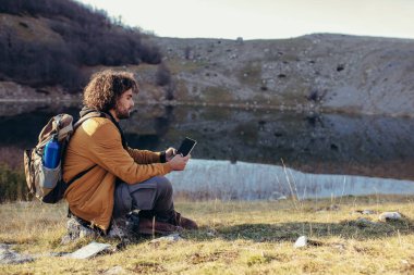 Lake yakınındaki otururken harita üzerinde modern dijital tablet doğa üzerinde eğitim düşünceli genç adam