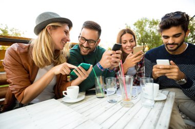 Grup dört arkadaşıyla birlikte bir kahve eğleniyor. İki kadın ve iki erkek gülüyor ve onların zaman zevk kafede. Telefon kullanma 