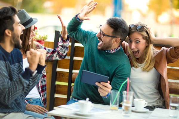 Grup dört arkadaşıyla birlikte bir kahve içer. İki kadın ve iki erkek gülüyor ve dijital tablet kullanarak zamanlarını zevk Café.