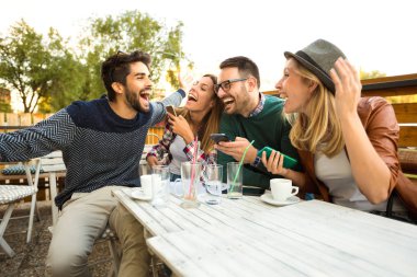 Grup dört arkadaşıyla birlikte bir kahve eğleniyor. İki kadın ve iki erkek gülüyor ve onların zaman zevk kafede. Telefon kullanma 