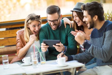 Grup dört arkadaşıyla birlikte bir kahve içer. İki kadın ve iki erkek gülüyor ve dijital tablet kullanarak zamanlarını zevk Café.