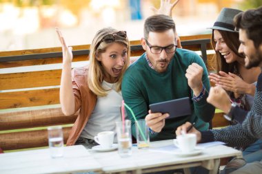 Grup dört arkadaşıyla birlikte bir kahve içer. İki kadın ve iki erkek gülüyor ve dijital tablet kullanarak zamanlarını zevk Café.