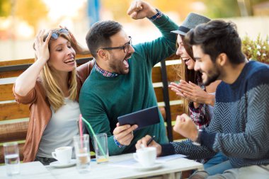 Grup dört arkadaşıyla birlikte bir kahve içer. İki kadın ve iki erkek gülüyor ve dijital tablet kullanarak zamanlarını zevk Café.