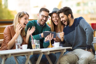 Grup dört arkadaşıyla birlikte bir kahve içer. İki kadın ve iki erkek gülüyor ve dijital tablet kullanarak zamanlarını zevk Café.