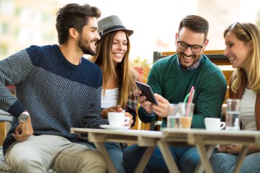 Grup dört arkadaşıyla birlikte bir kahve içer. İki kadın ve iki erkek gülüyor ve dijital tablet kullanarak zamanlarını zevk Café.