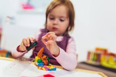Çocuk kız çocuk odası Oda masada otururken hamuru ile oynuyor.