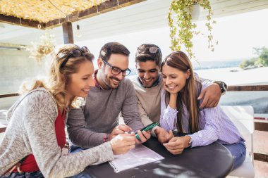 Grup dört arkadaşıyla birlikte bir kahve eğleniyor. İki kadın ve iki erkek gülüyor ve akıllı telefon kullanarak Café.